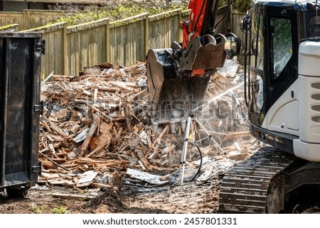Demolition cleanup and debris removal, heavy equipment with jawbone bucket, sprinkler used to keep dust down and under control, residential construction
 Royalty-Free Stock Photo #2457801331