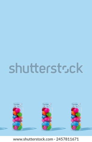 A pattern of glass bottles full of colorful candies on a blue background with copy space.
