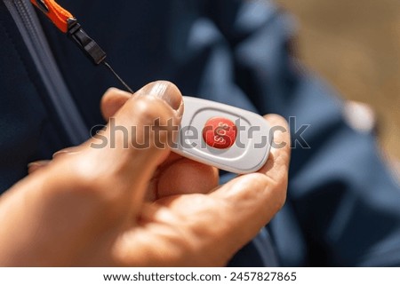 hand activating a red SOS emergency button on a safety device, attached to a jacket with an orange lanyard. Dementia retirement home concept image Royalty-Free Stock Photo #2457827865