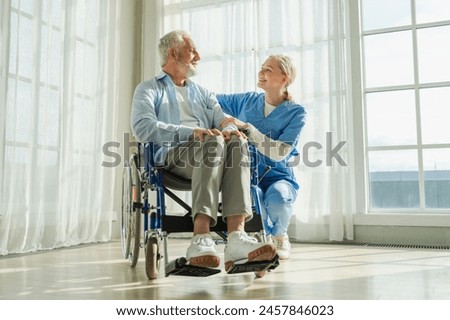 Help support retirement healthcare. Nurse helping old man in wheelchair. Patient and woman in nursing home for medical caregiver. Nurse taking care of paralyzed man in chair for people with disability Royalty-Free Stock Photo #2457846023