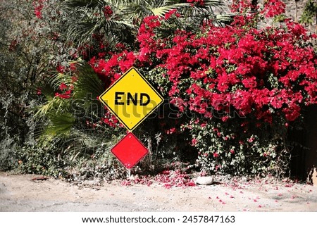 "END" road sign amidst vibrant red bougainvillea and lush greenery.