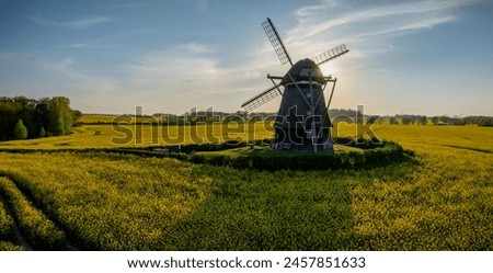 Historic mill amidst a rapeseed field, in the glow of the evening sun at sunset. Spring landscape with bright yellow rapeseed field and an old windmill by evening. Royalty-Free Stock Photo #2457851633