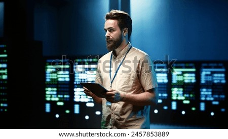 Worker doing yearly system reconditioning, imputing data on tablet of required patching in server cabinets housing advanced data storage equipment supporting critical IT workloads Royalty-Free Stock Photo #2457853889