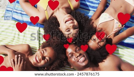 Image of red hearts over smiling african american family on holiday lying on beach towels. family, holidays, love and togetherness concept digitally generated image.