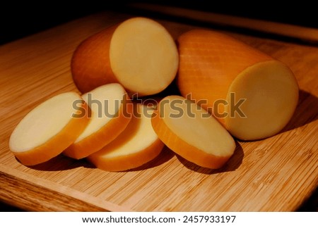 SMOKED PROVOLONE CHEESE IN A ROLL ON BOARD WITH CHOPPED PART IN FRONT ON ISOLATED WHITE BACKGROUND Royalty-Free Stock Photo #2457933197