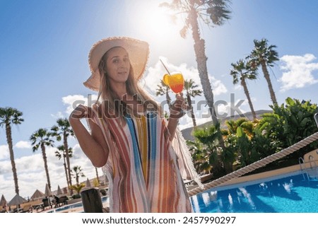 Smiling woman in a straw hat and colorful cover-up holding a tropical cocktail at a sunny poolside at caribbean island hotel 