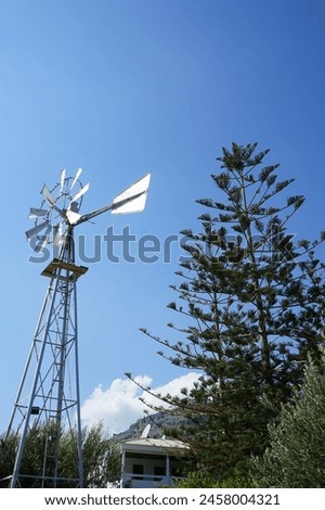 A weather vane is placed in the garden in August in Pefki. A wind vane, weather vane, or weathercock is an instrument used for showing the direction of the wind. Pefkos or Pefki, Rhodes Island Royalty-Free Stock Photo #2458004321