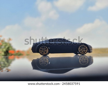 Matt black car with reflection in broad daylight with beautiful background of clouds hill and tree with orange flowers elevating the foreground object the star of the picture.
