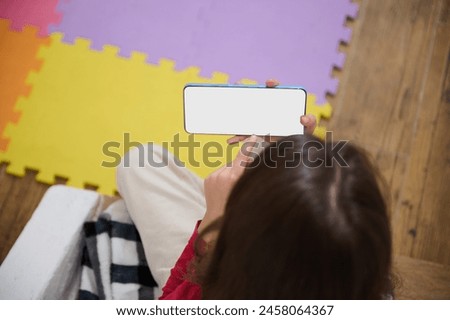 View from above of little kid's hands holding smart mobile phone with blank white empty digital touch screen. Mockup. Copy space for mobile application or advertising text. People. Wireless technology