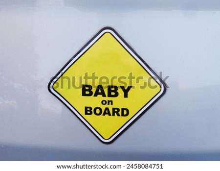 Simple yellow and black "Baby on board" caution sticker on the grey car with empty space