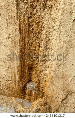 The flow of water on the farm along the adobe wall, old beaten cobwork, build with earth blocks. Plaster with an admixture of straw Royalty-Free Stock Photo #2458101317