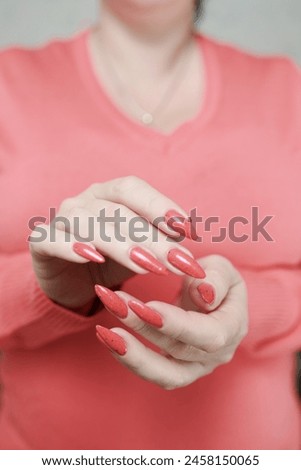 Female hand with long nails and a bright coral orange manicure holds a bottle of nail polish