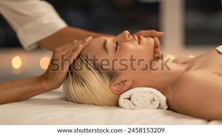 The photo shows a blonde woman lying down during a facial massage at a spa, with a calm and peaceful expression, enhancing her youthful glow