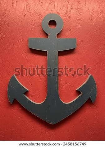 A black wall hanging in the shape of a boat anchor, handing on a bright red wall.