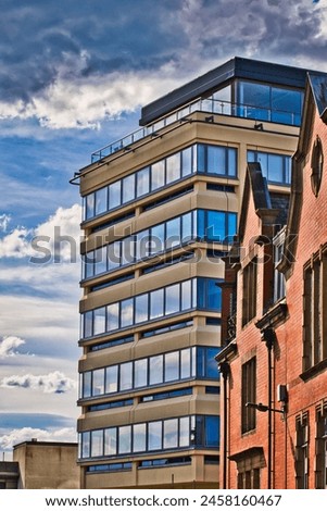 Modern glass building juxtaposed against a traditional brick building under a dynamic cloudy sky. Royalty-Free Stock Photo #2458160467