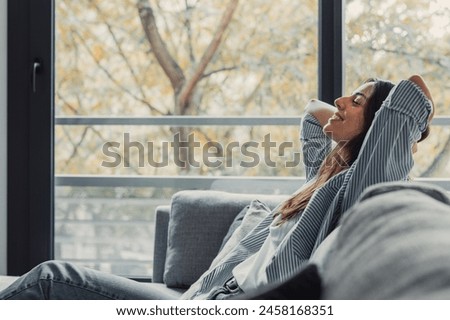 Relaxed serene pretty young woman feel fatigue lounge on comfortable sofa hands behind head rest at home, happy calm lady dream enjoy wellbeing breathing fresh air in cozy home modern living room Royalty-Free Stock Photo #2458168351