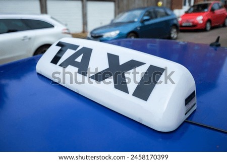 Taxi sign on the top of a blue motor vehicle parked on an urban street