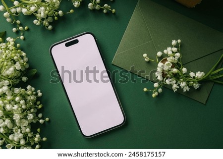 Phone in hands with isolated screen on the background of lilies of the valley.