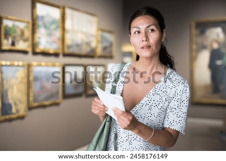 Adult Asian woman standing in picture gallery and watching exposition