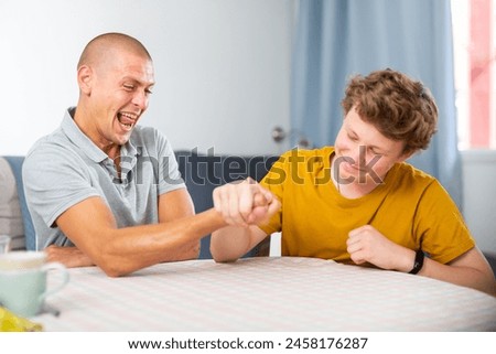 Father arm wrestling his son. They're happy and havung fun.