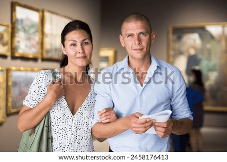 Wife and husband standing in picture gallery and watching paintings