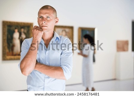 Adult European man standing in picture gallery and watching exposition