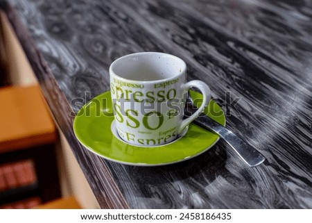 A green-and-white espresso cup with espresso written on it and a spoon on the side.