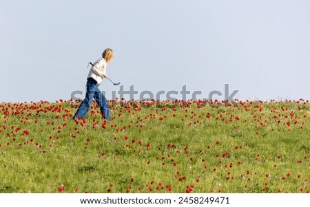A woman takes a photo of a field with red tulips in spring on her phone.