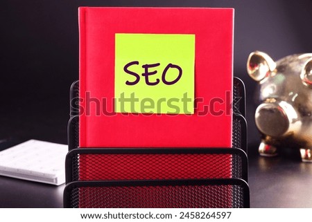 SEO business, SEO concept. Search engine optimization text on a yellow sticker glued to a red business notebook on a black background