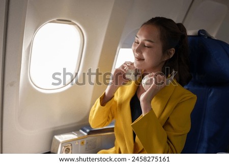 A business woman in a yellow suit is having fun. Happy using headphones to listen to music online on an airplane with a Wi-Fi internet connection. Business travel.