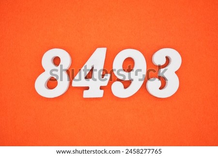 The number 8493 is made from white painted wood placed on a background of orange paper.