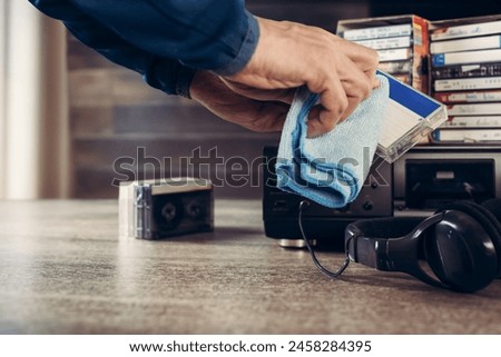 Male hands wiping old tape cassette from dust, closeup photo. Audio equipment: Antique cassette player and cassettes, suitable for retro audio concepts