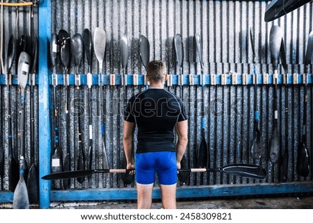 Rear view of young canoeist standing in front of wall with paddles. Concept of canoeing as dynamic and adventurous sport. Royalty-Free Stock Photo #2458309821