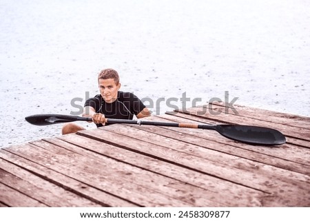 Canoeist man sitting in canoe holding paddle, getting out of water. Concept of canoeing as dynamic and adventurous sport. Royalty-Free Stock Photo #2458309877