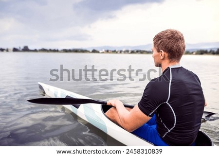 Canoeist man sitting in canoe holding paddle, in water. Concept of canoeing as dynamic and adventurous sport. Rear view, sportman looking at water surface, paddling Royalty-Free Stock Photo #2458310839