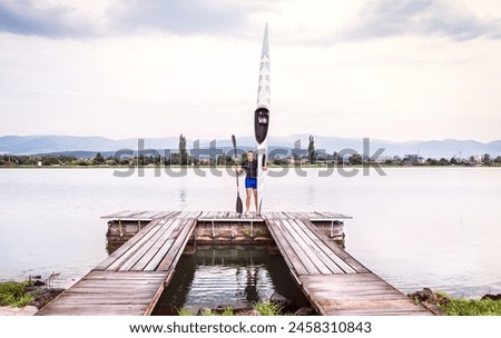 Young canoeist holding canoe and paddle, going into water, wstanding on wooden dock. Concept of canoeing as dynamic and adventurous sport Royalty-Free Stock Photo #2458310843