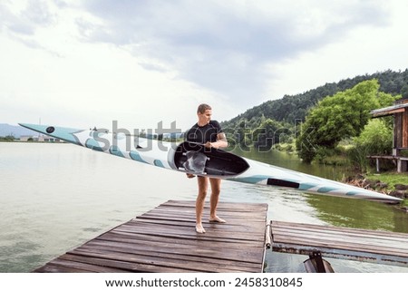 Young canoeist carry canoe and paddle, going into water, walking on wooden dock. Concept of canoeing as dynamic and adventurous sport Royalty-Free Stock Photo #2458310845