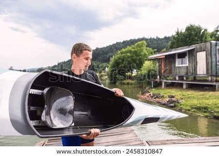 Young canoeist carry canoe and paddle, going into water, walking on wooden dock. Concept of canoeing as dynamic and adventurous sport Royalty-Free Stock Photo #2458310847