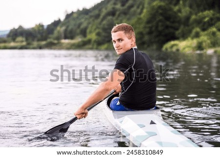 Canoeist man sitting in canoe holding paddle, in water. Concept of canoeing as dynamic and adventurous sport. Rear view, sportman looking at water surface, paddling Royalty-Free Stock Photo #2458310849