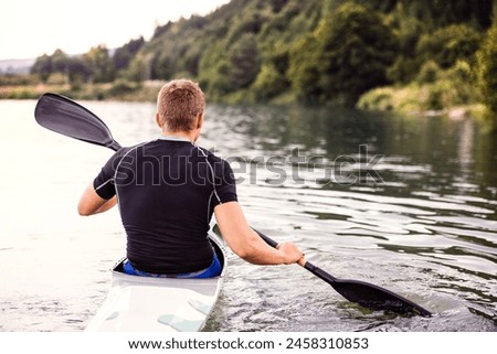 Canoeist man sitting in canoe holding paddle, in water. Concept of canoeing as dynamic and adventurous sport. Rear view, sportman looking at water surface, paddling Royalty-Free Stock Photo #2458310853