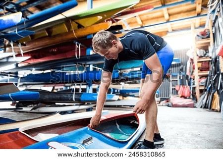 Young canoeist preparing canoe and paddle, going on water. Concept of canoeing as dynamic and adventurous sport. Royalty-Free Stock Photo #2458310865