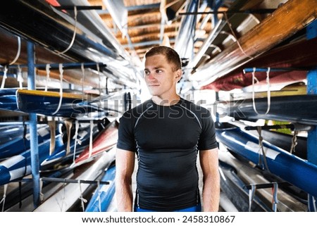 Portrat of young canoeist standing in the middle of stacked canoes. Concept of canoeing as dynamic and adventurous sport. Royalty-Free Stock Photo #2458310867