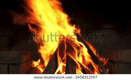 The roaring fire, with its orange glow, stands tall against the dark brick wall, creating a cozy atmosphere in the chilly night. Royalty-Free Stock Photo #2458312597
