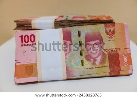 Several stacks of new IDR 100,000 (Indonesian Rupiah) banknotes, on white paper with cream background, stock photo.