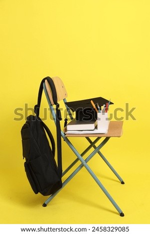 Back to school concept with school books, textbooks, backpack and stationery supplies on classroom chair isolated on yellow background. Studying abroad, Gen Z, E-learning.
