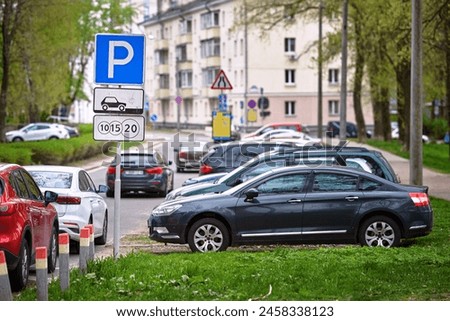 Car parked under green trees in residential area on paid parking zone. Crowded public parking lot. Parking lot sign in residential area, indicating paid parking zone
