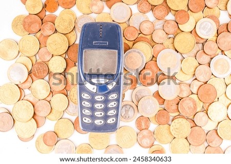 A cell phone is sitting on top of a pile of coins. The coins are of various sizes and colors, and they are scattered all over the phone. The scene gives off a sense of clutter and real image