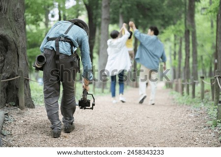 A cameraman takes a picture of a Japanese family walking through fresh greenery with his camera on a gimbal.