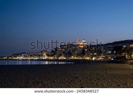 Twilight over a calm beach, city lights and a lit cathedral in the background, peaceful evening scene. High quality photo
