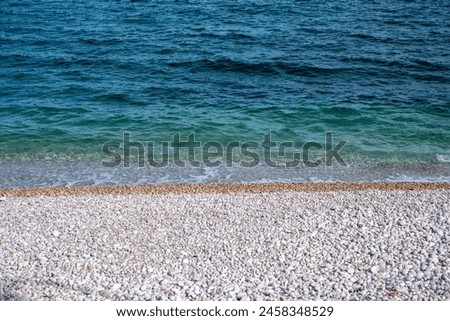 A serene pebble beach meets the clear, tranquil waters of a calm sea, epitomizing peaceful natural coastlines. High quality photo